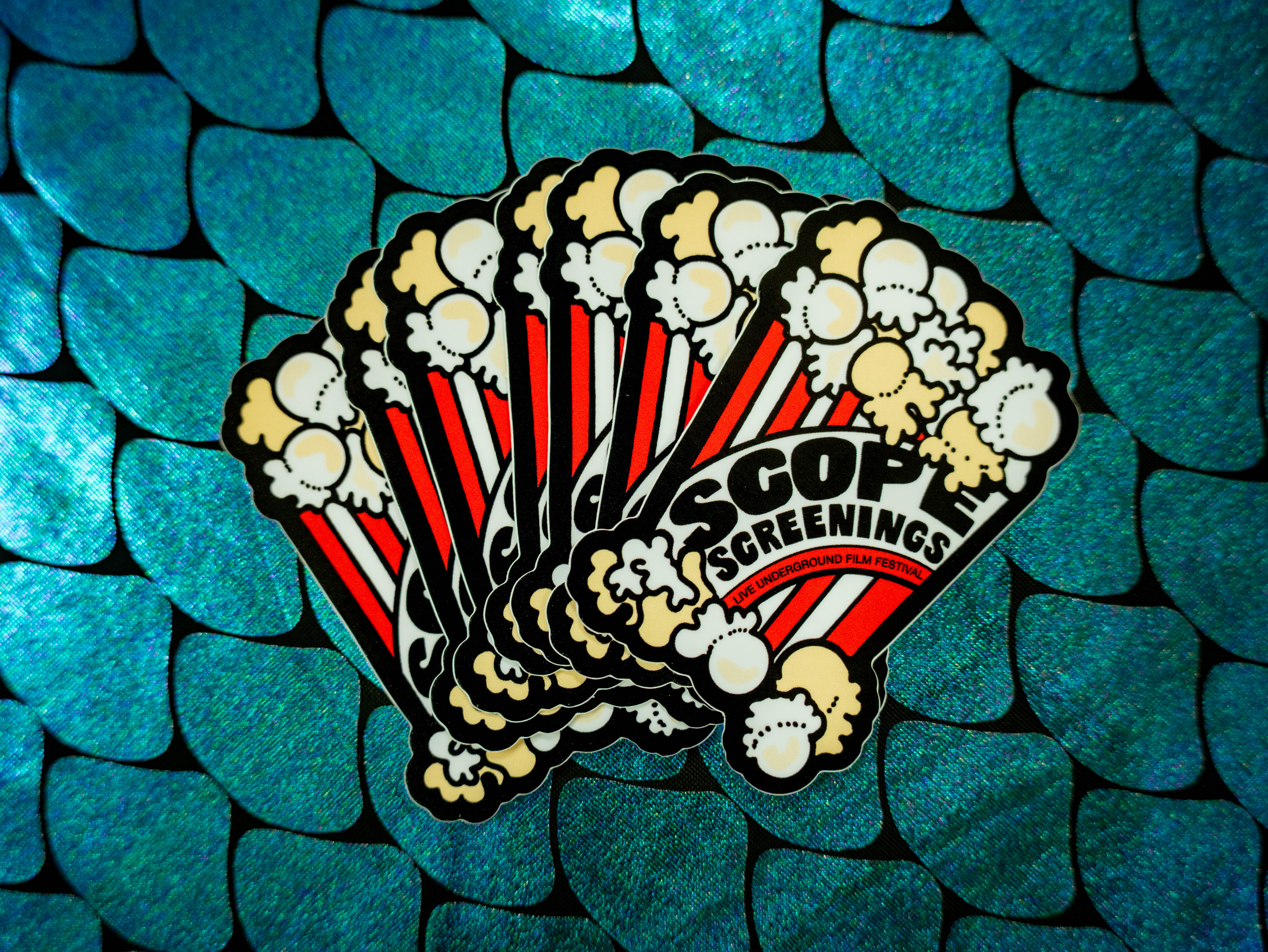 Scope Screenings branded stickers — product flat-lay on teal mermaid-scale background